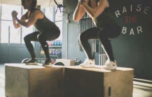 Two women working out squat on boxes